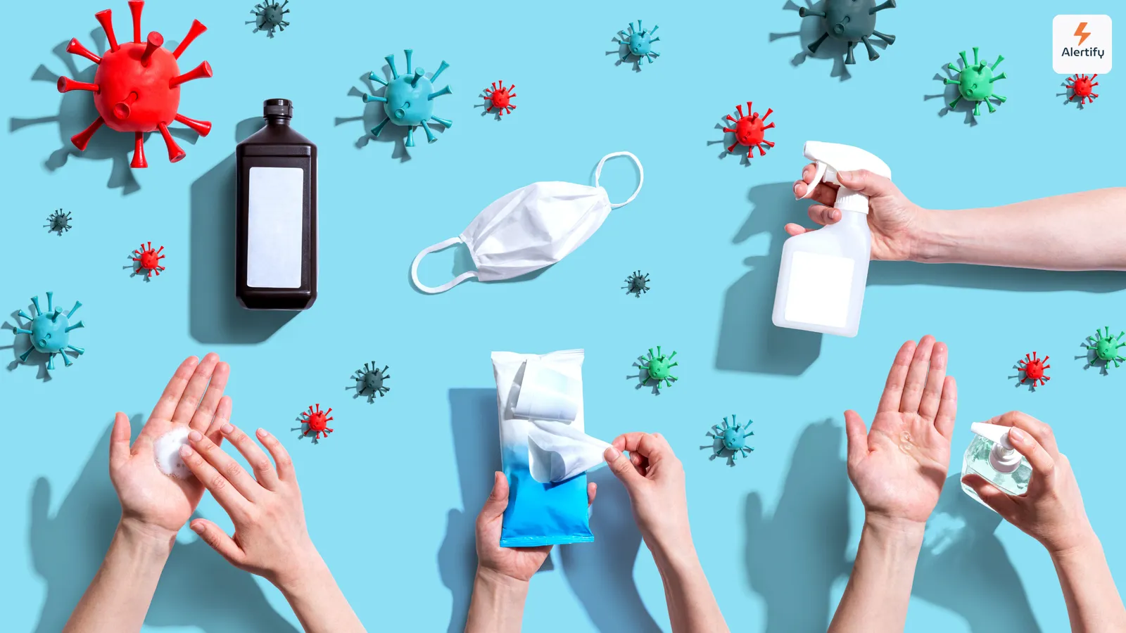 Draufsicht auf Virusmodelle, eine Schutzmaske, Desinfektionsspray und Hände mit Hygieneprodukten