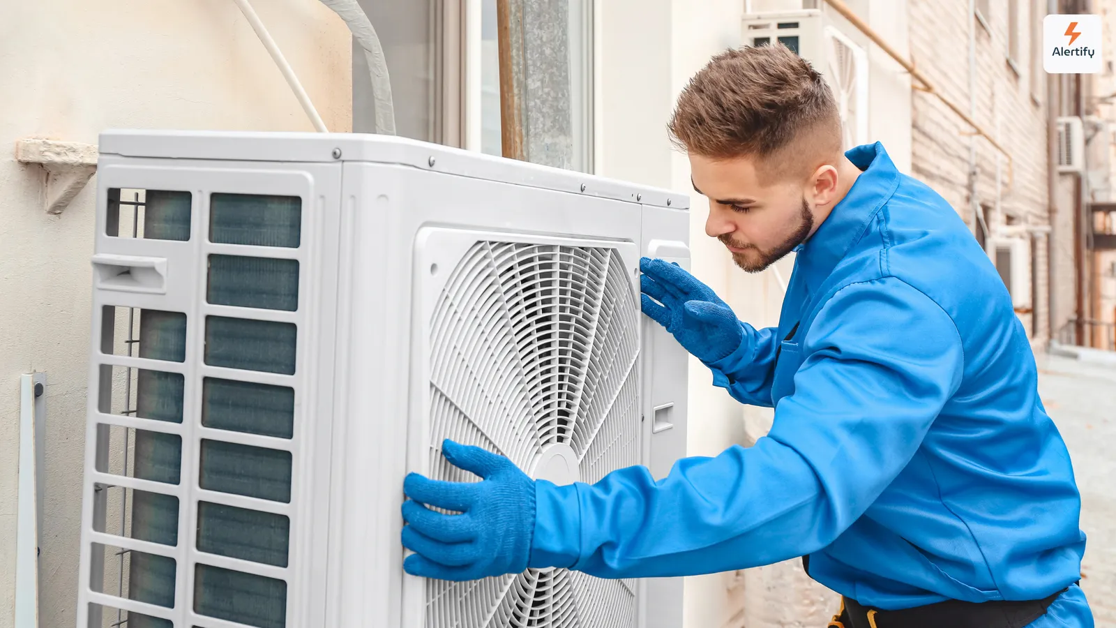 HLK-Techniker in blauem Overall und Handschuhen wartet ein Klimaaußengerät