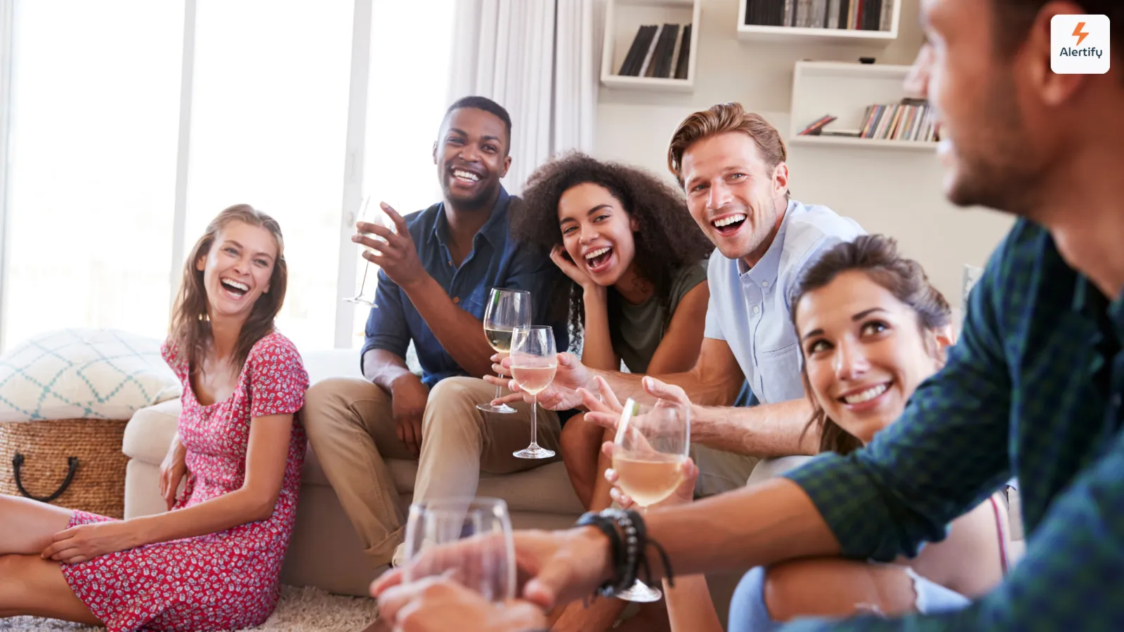 Gruppe von Freunden, die im Wohnzimmer einer Ferienwohnung lachend Wein trinkt