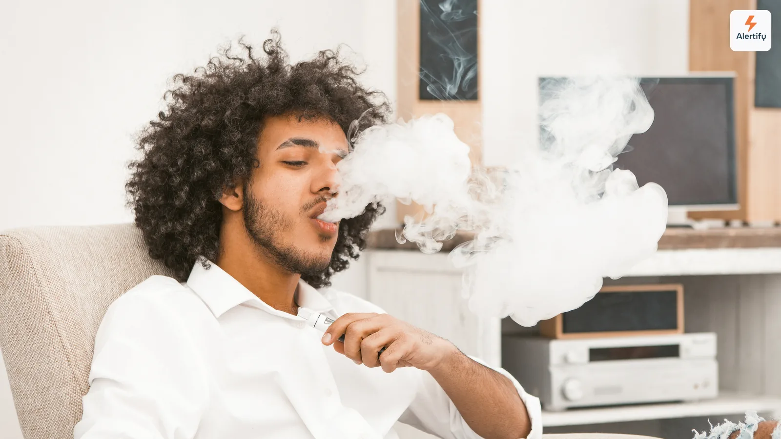 Gast stößt eine dicke Dampfwolke aus, während er im Wohnzimmer einer Ferienwohnung sitzt