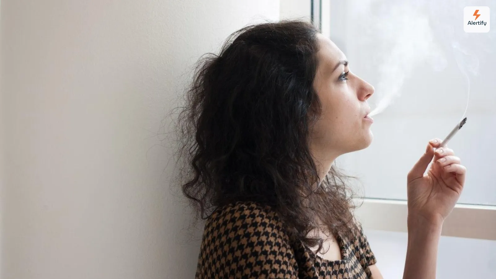 Gast lehnt an einer Wand und raucht drinnen eine Zigarette neben einem hellen Fenster in einer Ferienwohnung
